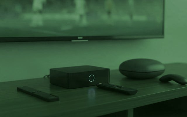 A streaming stick, a set-top box and a round streaming box with their remotes on a TV console