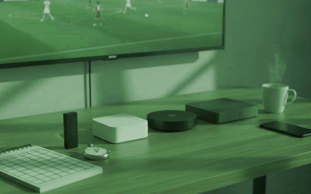 Five streaming devices, a notebook scoring grid and a stopwatch in front of a TV showing a football match