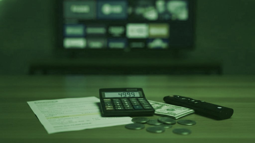 A calculator, dollar bills, coins, a streaming stick and a remote on a table in front of a TV